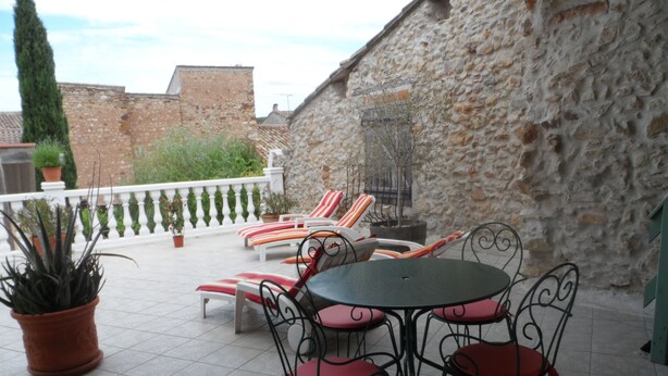 A terrace with a stone wall, lounge chairs, a table, and potted plants. - Clos Mazerolles (Cruzy)