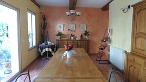 A dining area with a wooden table, chairs, a vase of flowers, a cabinet, and a window. - Clos Mazerolles (Cruzy)