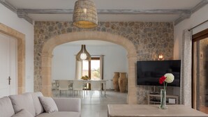 Ein modernes Wohnzimmer mit einer Couch, einem Couchtisch und einem Fernseher. Eine Steinwand und ein Durchgang führen in einen Essbereich.