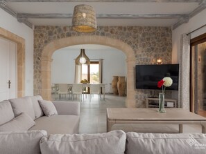 A modern living room with a sofa, a coffee table, and a TV. There is a stone wall and an archway leading to a dining area. - Villa Turquesa - Spectacular villa with pool and garden in Santa Margalida (Santa Margalida)