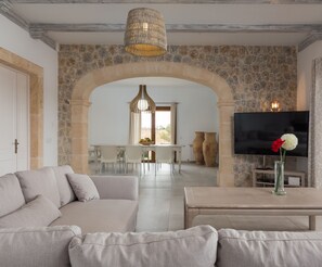 Un salon moderne avec un canapé, une table basse et un téléviseur. On y trouve un mur en pierre et une arche qui mène à un espace repas.