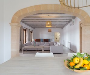 Un salon moderne avec une arche en pierre, un ensemble de canapés, une table à manger agrémentée d’un saladier de fruits et un luminaire suspendu.