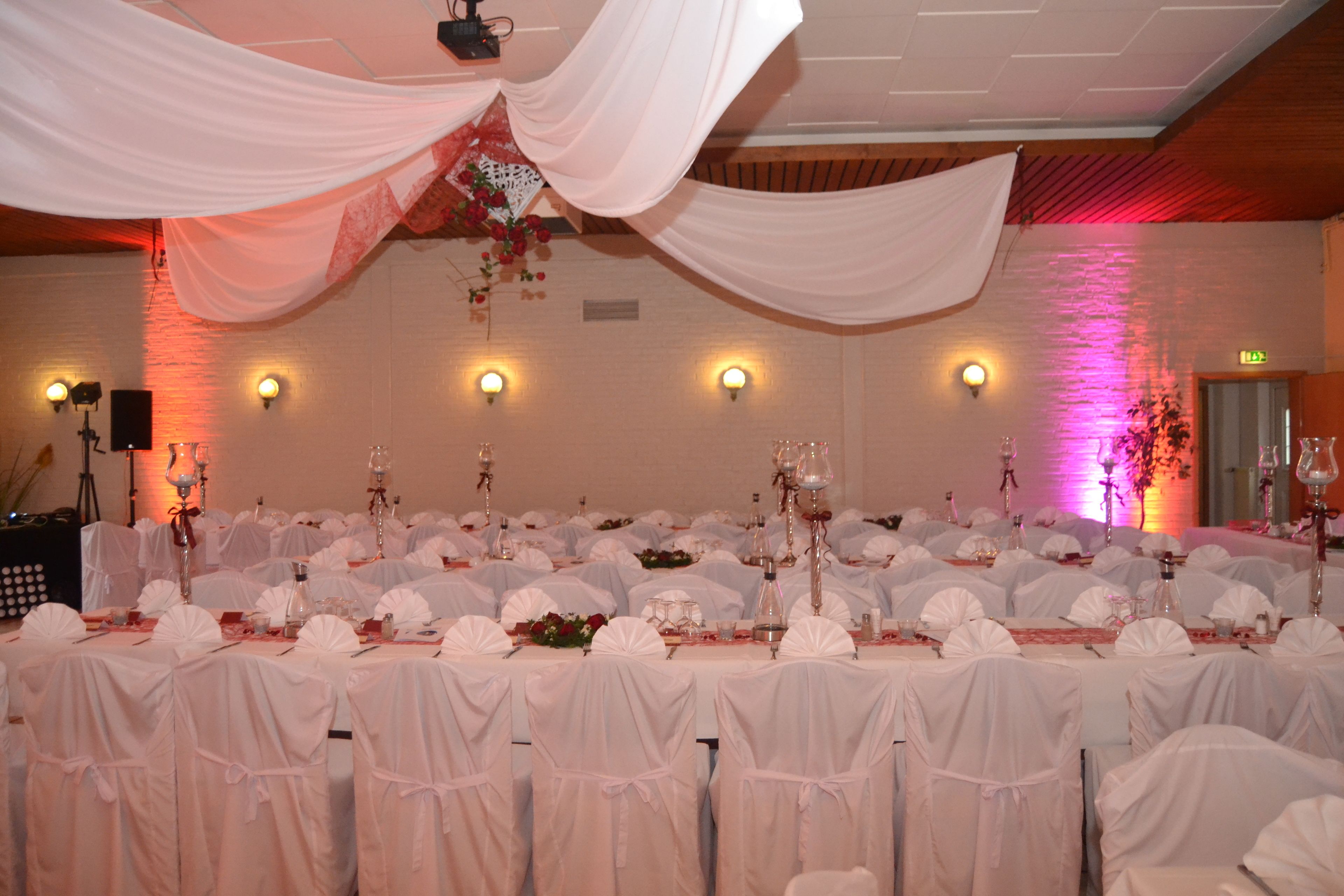 A banquet hall with tables set for a formal event, draped with white fabric and lit by wall sconces.