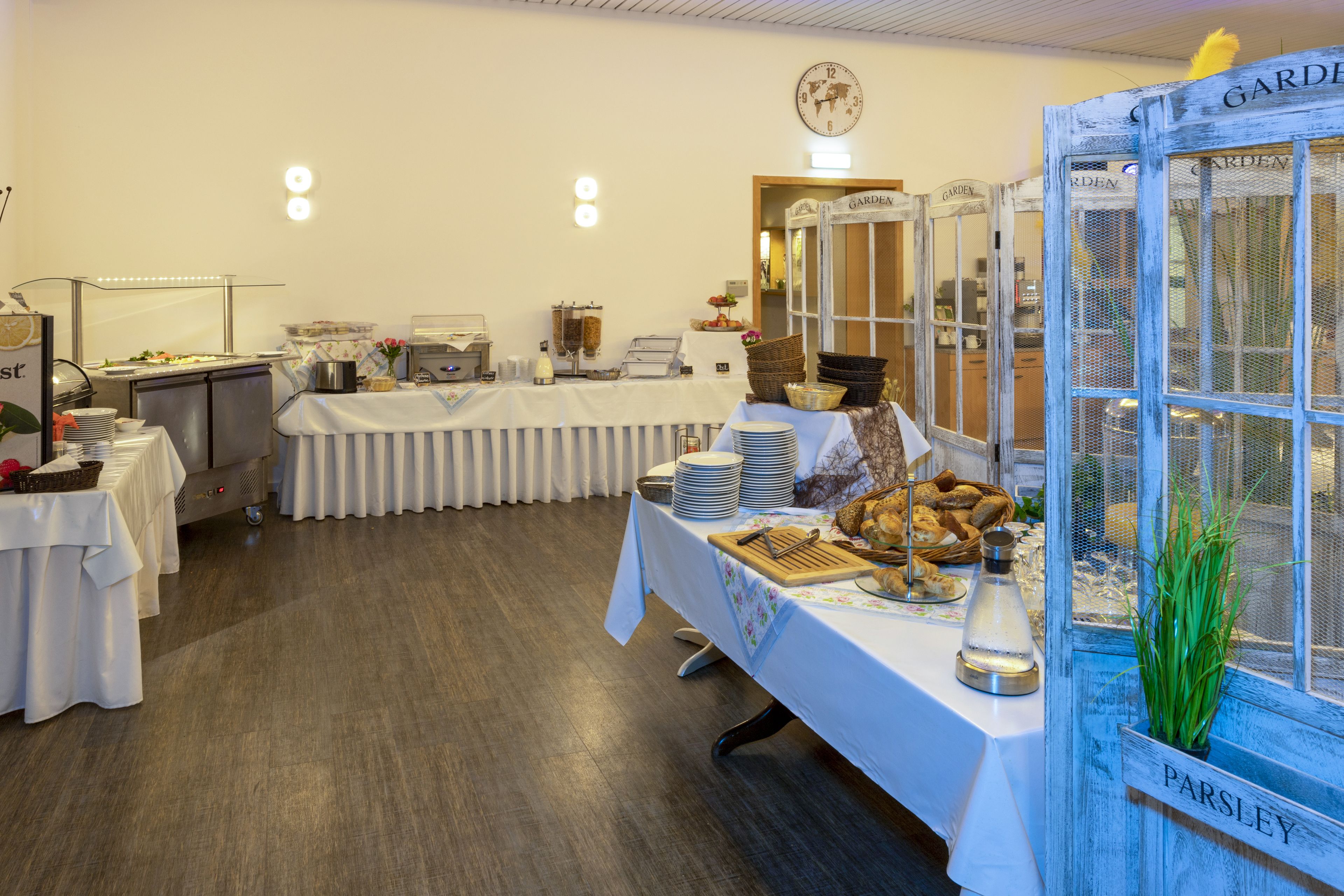 Ein Buffet mit mehreren Tischen, einer Wanduhr und einem Schild mit der Aufschrift 'Garden'.
