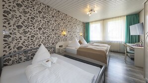 Een hotelkamer met twee bedden, een bureau, een televisie en een raam met gordijnen.