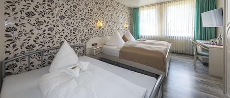 Una habitación de hotel con dos camas, un escritorio, un televisor y una ventana con cortinas.