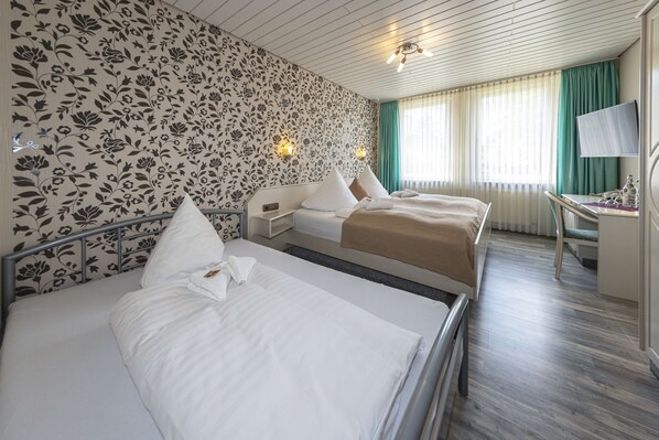 Una habitación de hotel con dos camas, un escritorio, un televisor y una ventana con cortinas.