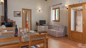 A cozy living room with a fireplace, a dining area with a table set for two, a television, and a striped sofa. - Son Fornes - Beautiful villa with pool and garden in Algaida (Algaida)