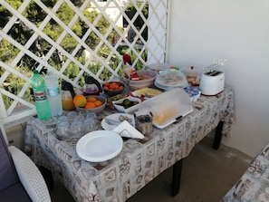A table set up with various food items and drinks, a toaster, and a plastic container on a patterned tablecloth. - Alla Vista Del Barocco (Lecce)