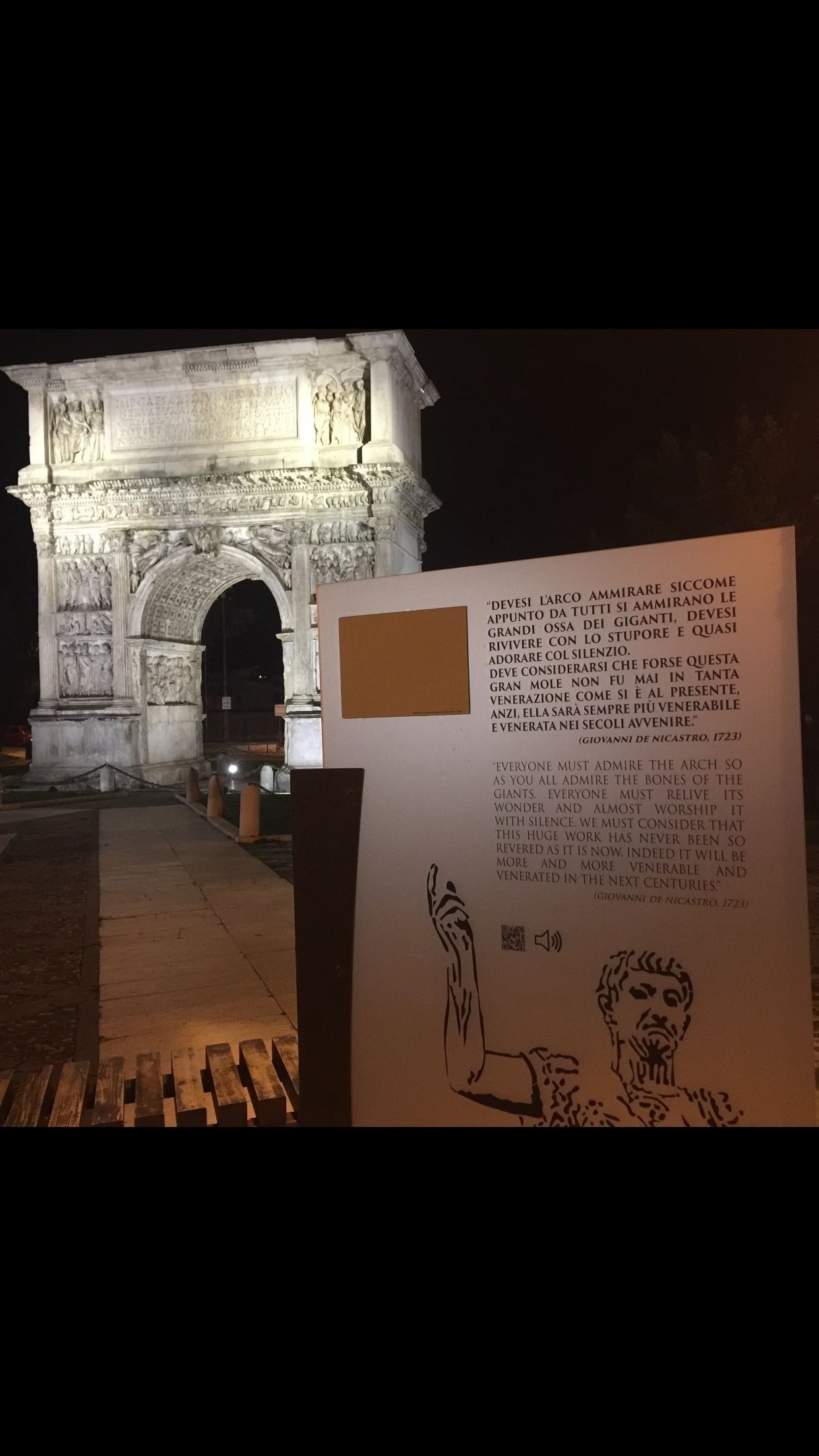 A historical monument at night with an informational plaque in the foreground.
