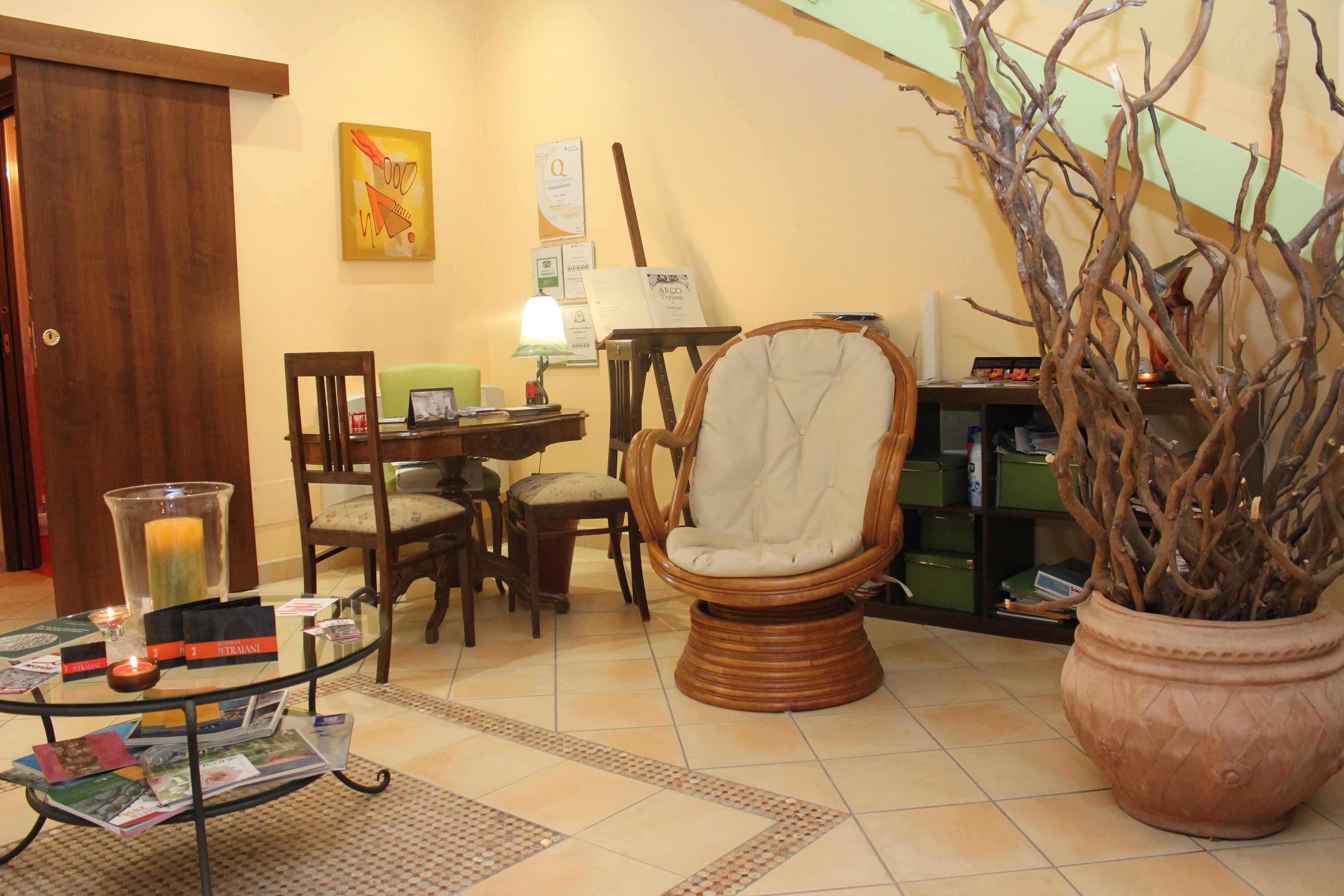 Uma sala de estar com mesa de centro de vidro, poltrona de vime e uma grande planta em vaso.
