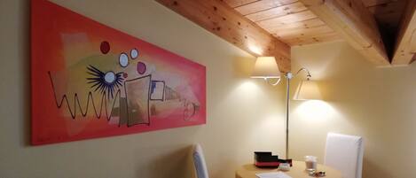A room with a wooden ceiling, a green sofa, a table with a lamp, and a colorful abstract painting on the wall.