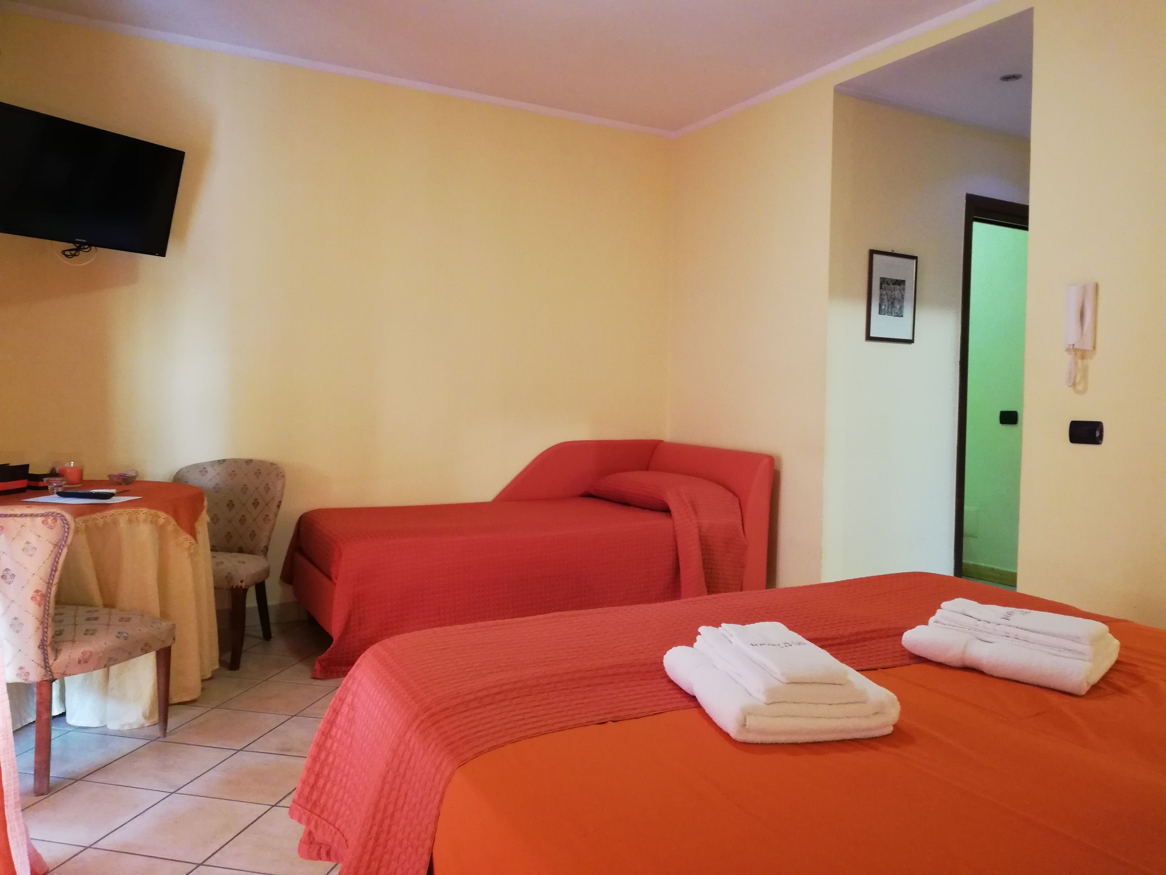 Una habitación de hotel con dos camas, un escritorio con una silla, un televisor y una puerta verde.
