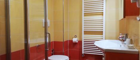 Un baño con ducha, dos inodoros, un lavabo y un perchero para toallas.