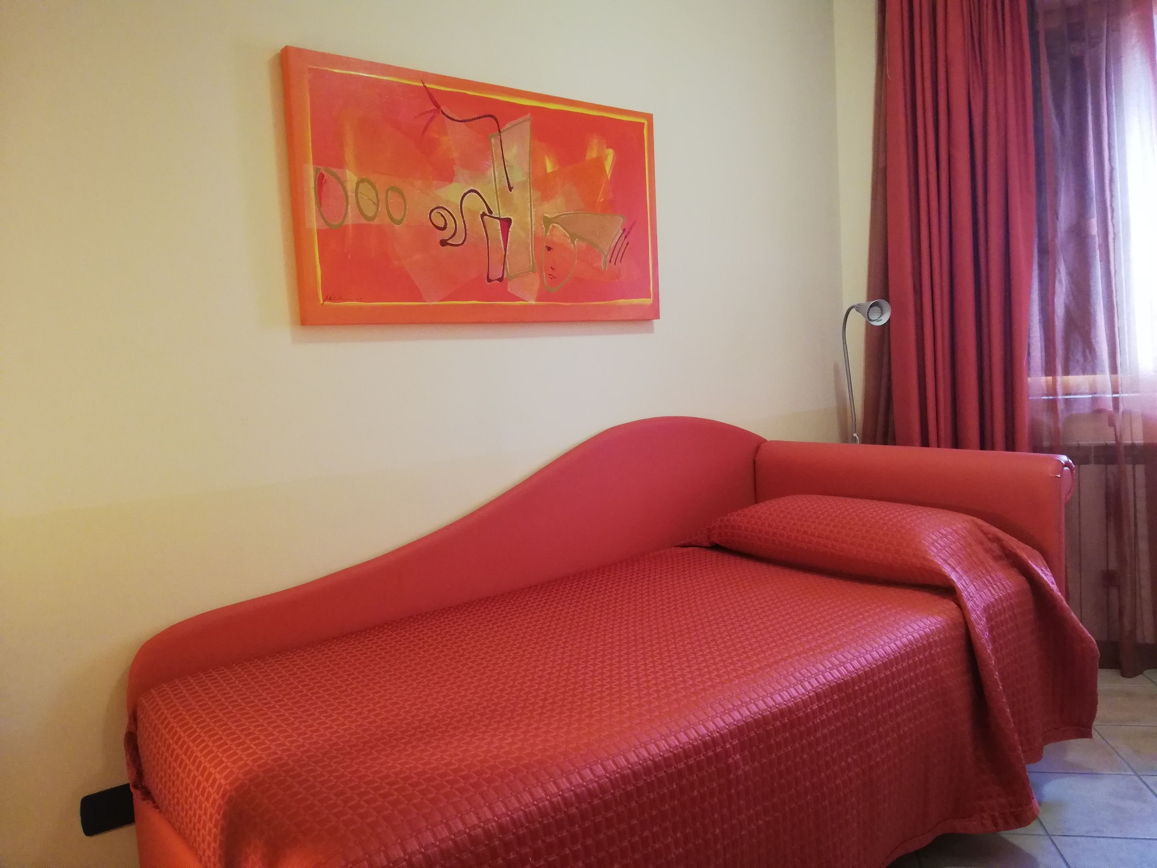 Een kamer met een rode bank, een schilderij aan de muur en een raam met gordijnen.
