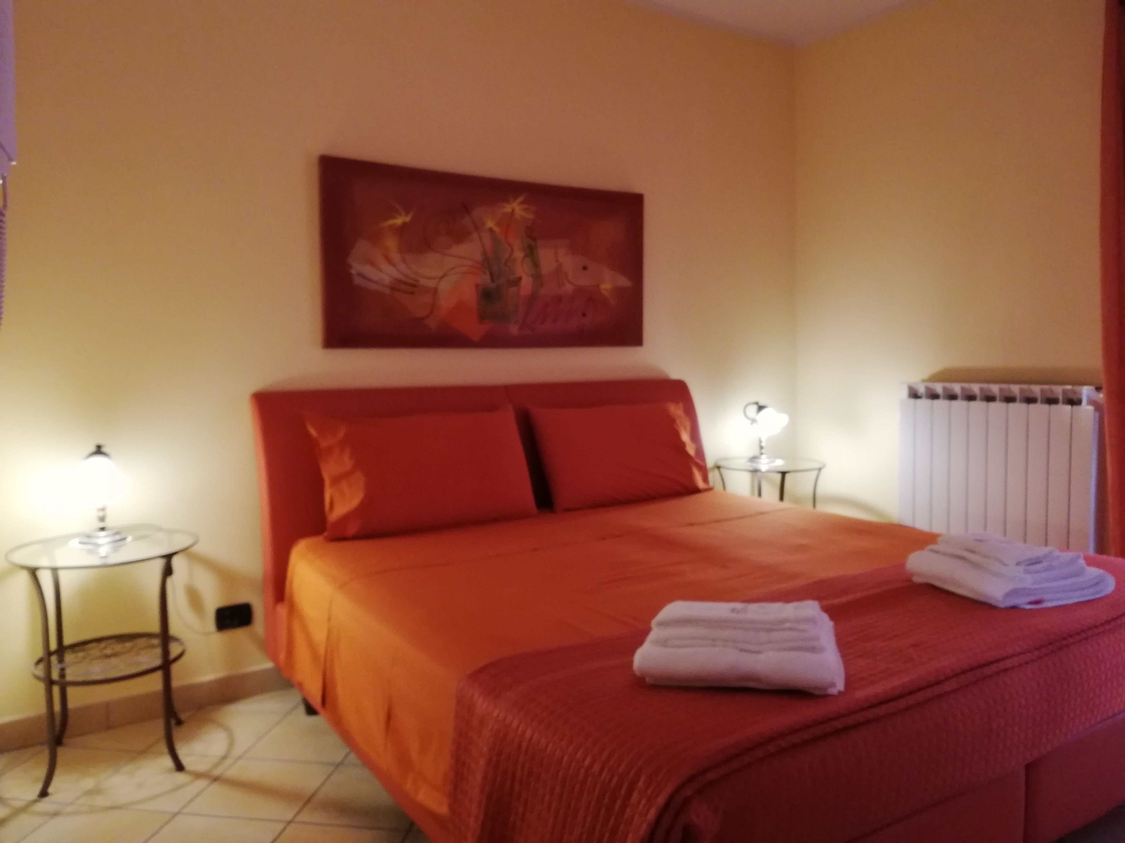 Ein Hotelzimmer mit einem großen Bett, zwei Nachttischen mit Lampen, einem Heizkörper und einem Gemälde an der Wand.