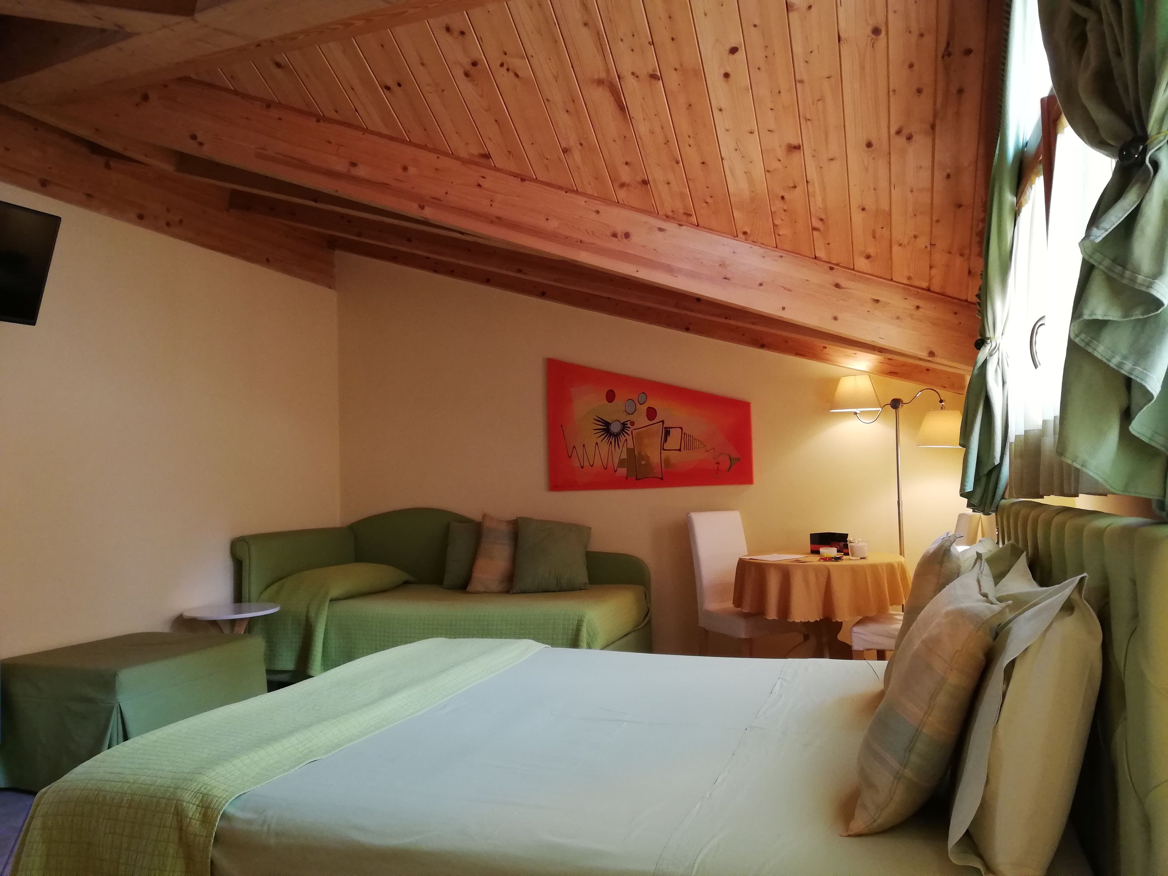 A cozy room with a bed, two green sofas, a small table, and a painting on the wall.