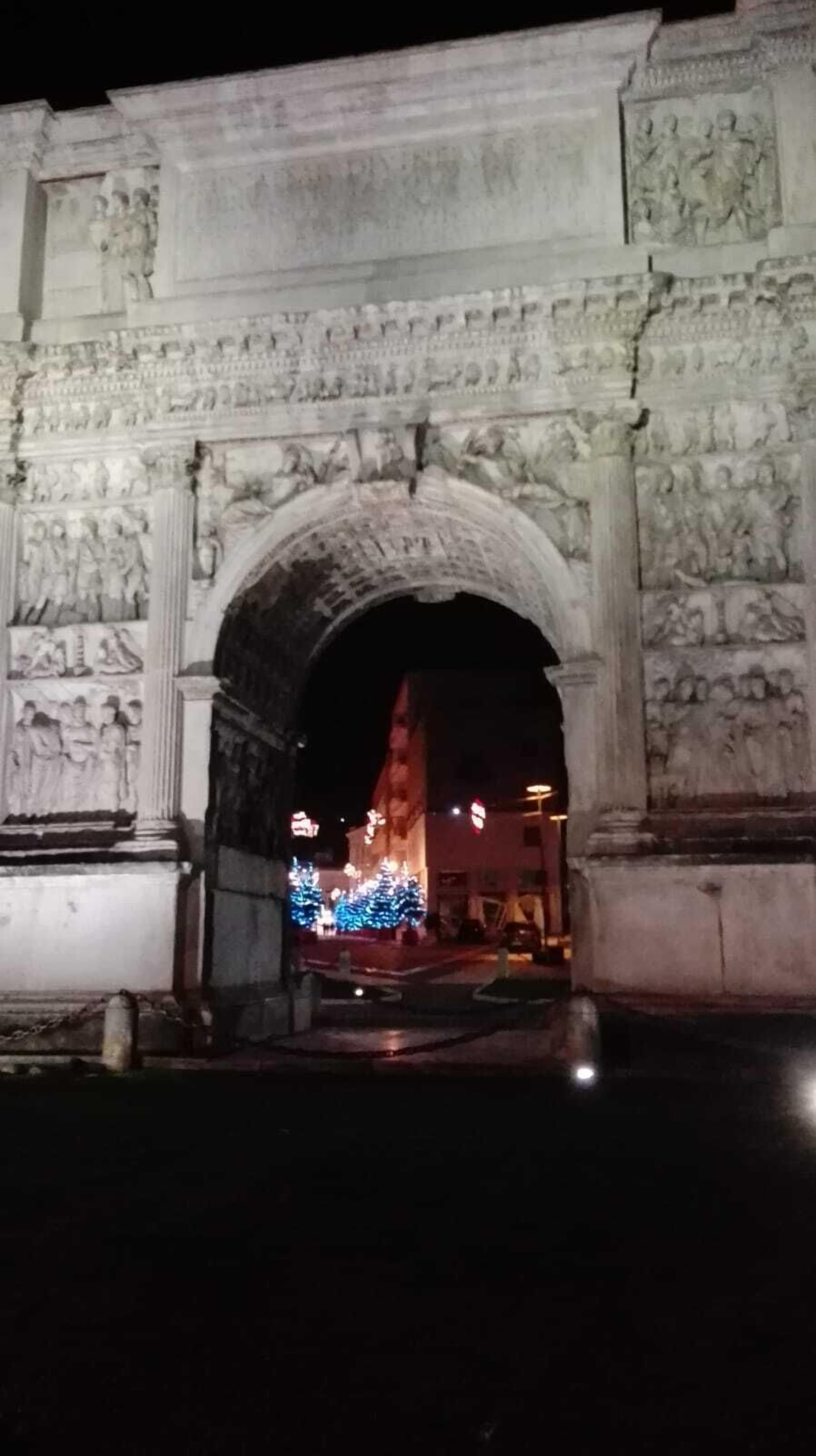 An ancient archway with detailed carvings and a Christmas tree decorated with lights.