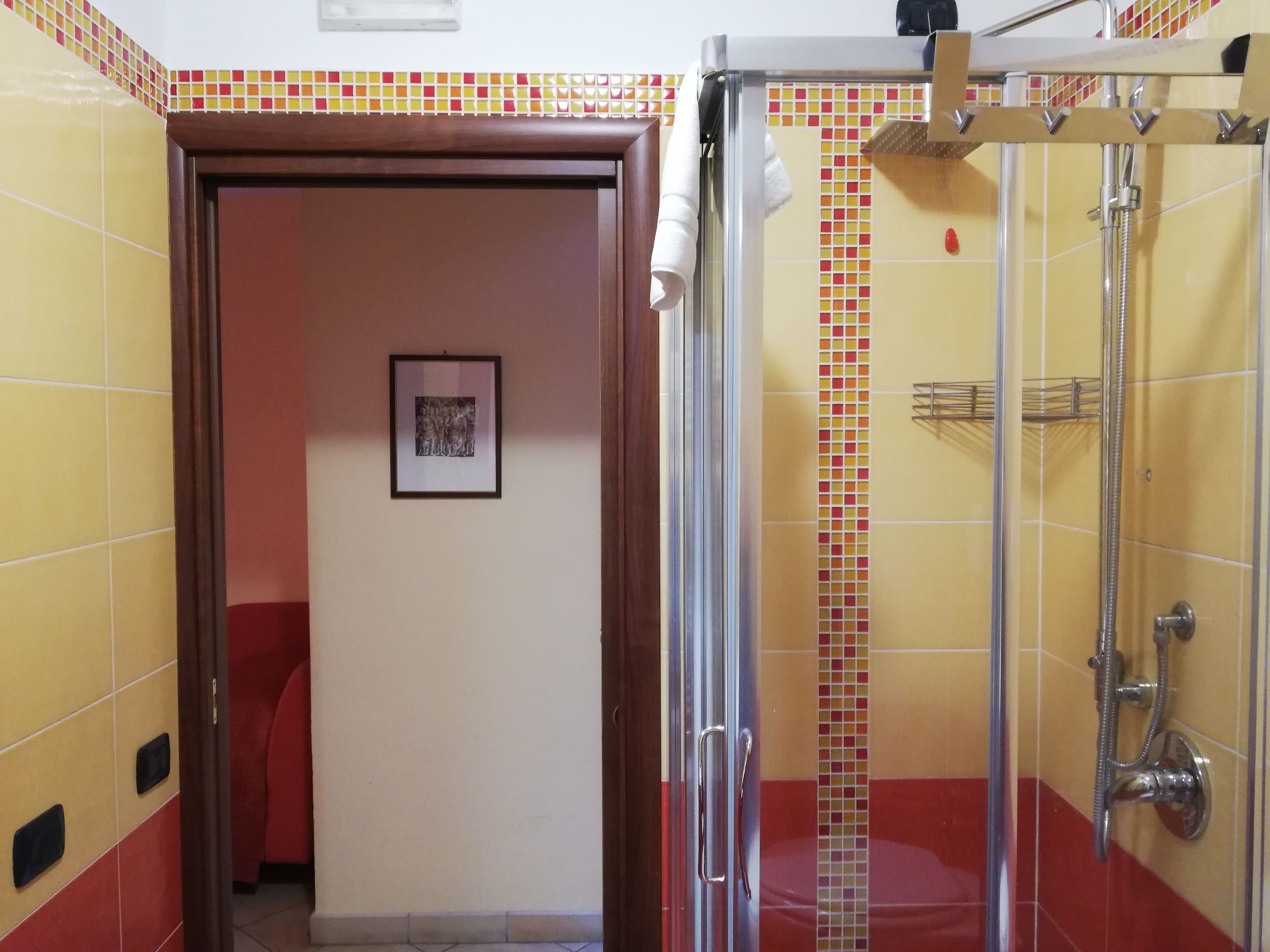 Un baño con baldosas amarillas y rojas, una ducha con puerta de cristal y un cuadro en la pared.