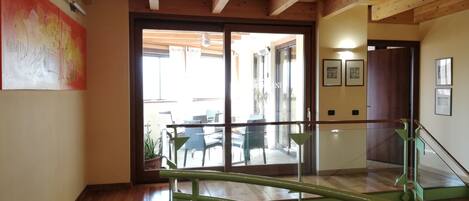 Et træinteriør med trappe, en glasdør der fører ud, og udsigt til udendørs siddepladser.