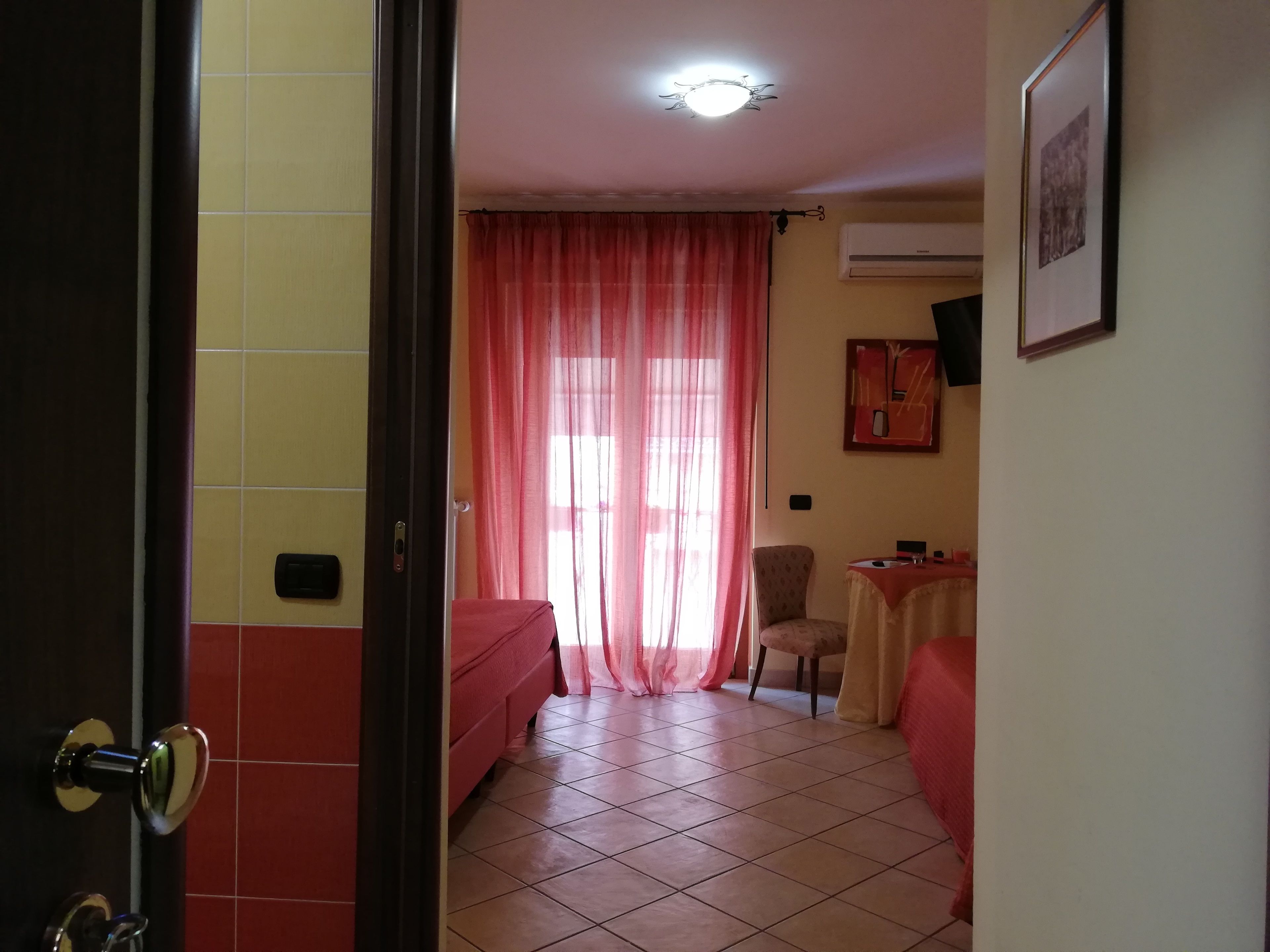 A hotel room with a bed, a chair, a small table, and a window with curtains.