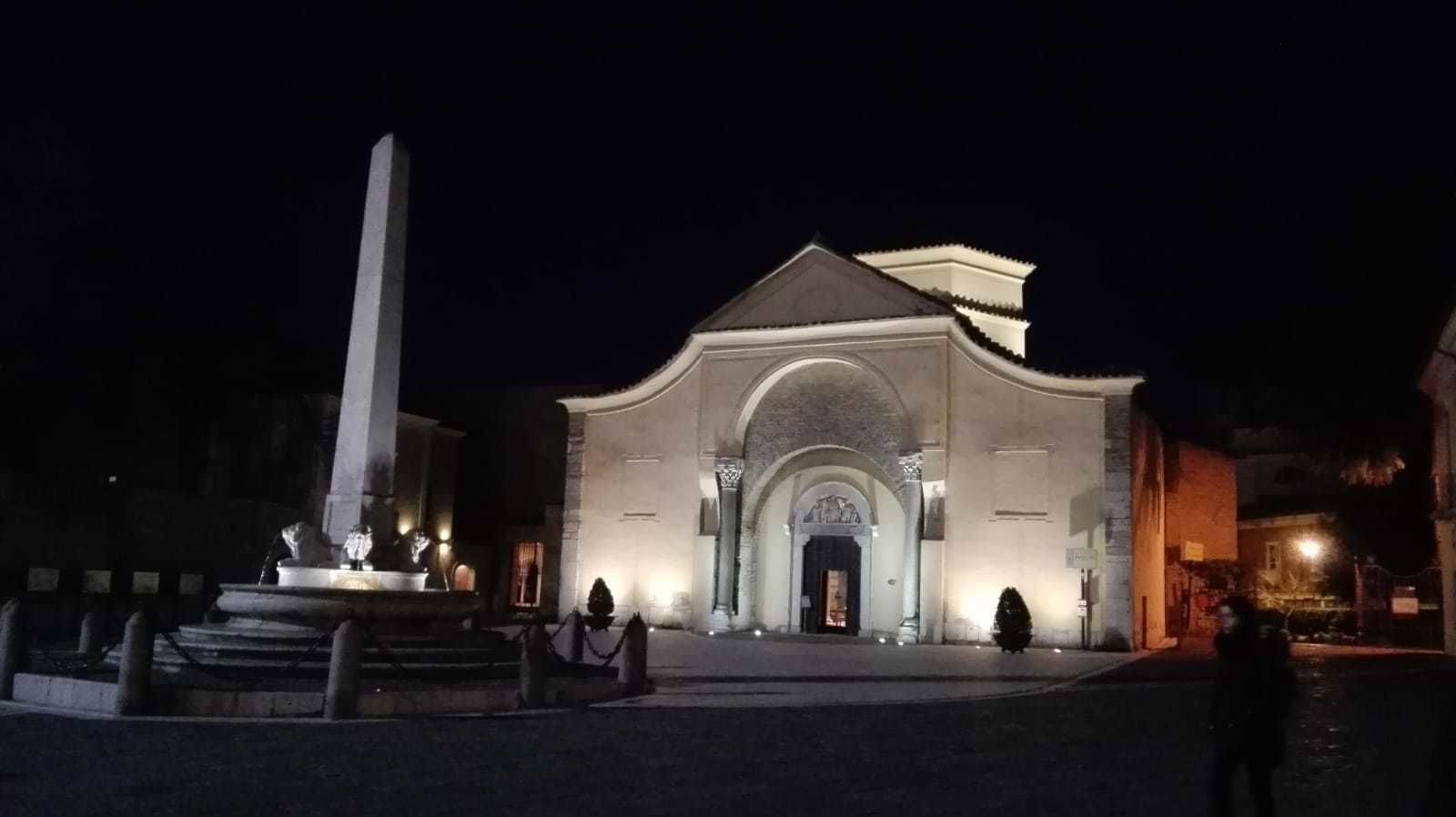 A historic building with a central archway and a tall obelisk in front.