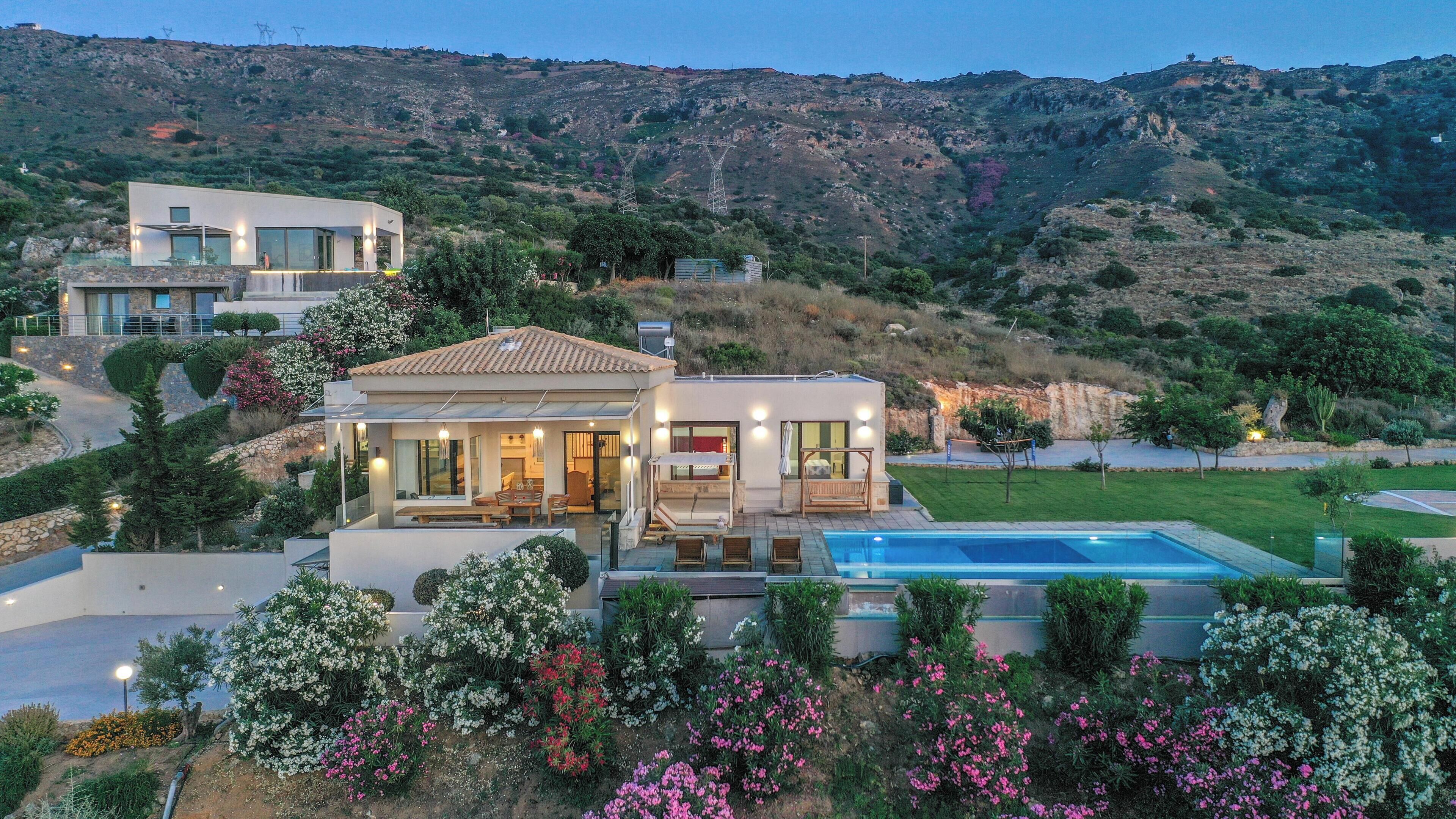 Une maison moderne dotée d’une piscine, entourée de jardins luxuriants et de collines.