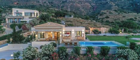 Une maison moderne dotée d’une piscine, entourée de jardins luxuriants et de collines.