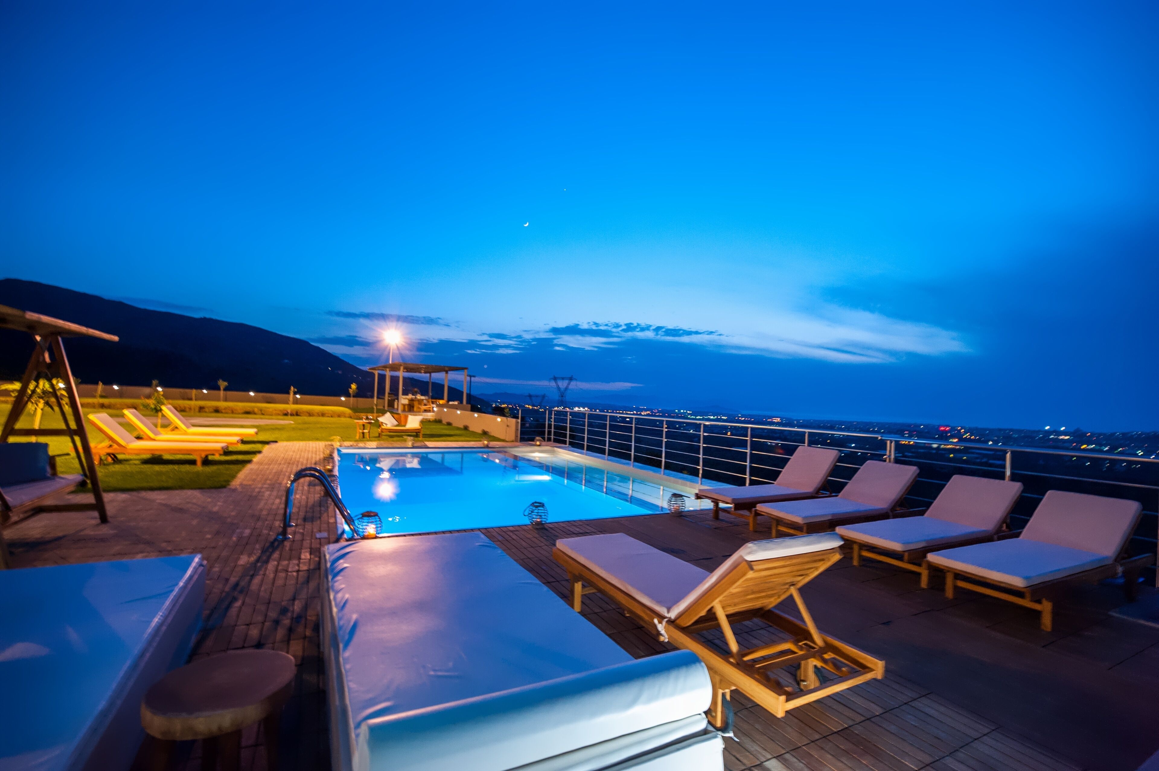 A rooftop pool area with lounge chairs and a view of the city at dusk.