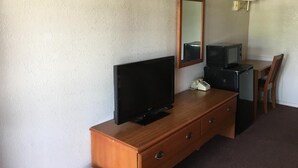Habitación de hotel con tocador de madera, televisor de pantalla plana, teléfono, microondas, mesita y una silla.