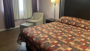 Una habitación de hotel con una cama grande, una silla, una mesita de noche y una lámpara.
