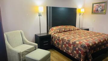 Un dormitorio con cama, una silla, un reposapiés, una mesita de noche y dos lámparas de pared.