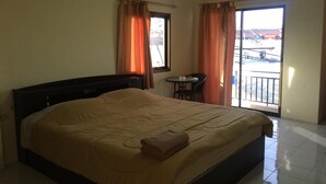 A hotel room with a large bed, a small table with a chair, and a balcony with a view of the city. - Kaesai Place (Pattaya)