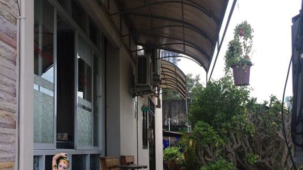 A covered outdoor seating area with a stone planter, wooden benches, and potted plants. - Kaesai Place (Pattaya)