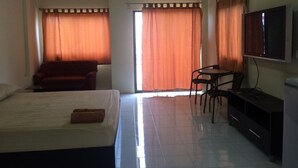 A hotel room with a bed, a desk, a chair, a television, and a window with curtains. - Kaesai Place (Pattaya)