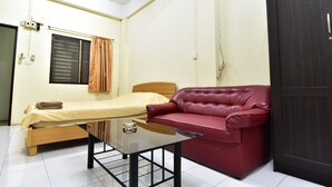 A small, clean room with a single bed, a red leather sofa, and a glass table. - Kaesai Place (Pattaya)