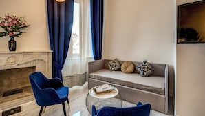 A living room with a sofa, a blue armchair, a small round table, and a vase of flowers. - Little Queen Pantheon Residence (Rome)