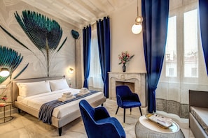 A modern bedroom with a large bed, a fireplace, and a seating area with blue chairs. - Little Queen Pantheon Residence (Rome)