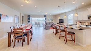 A spacious kitchen with a central island, dining area with chairs, and a living room with a sofa and TV.