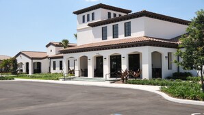A modern multi-story building with a white facade and terracotta roof tiles.