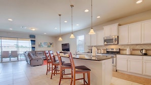 A spacious kitchen with white cabinets, a central island with bar stools, a built-in microwave, and a large window offering a view of the outdoors.