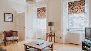 Un salon avec une table basse en bois, un fauteuil en osier, un téléviseur et une lampe sur une petite table.