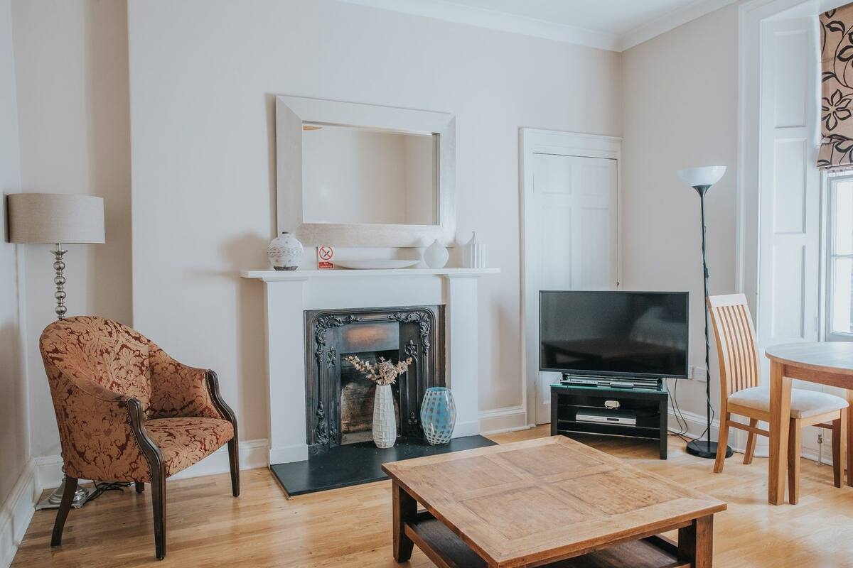 Ein Wohnzimmer mit Kamin, Fernseher, Couchtisch und einem gemusterten Sessel.