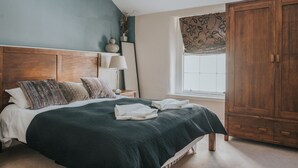Une chambre à coucher comprenant un lit, une table de chevet, une lampe, une fenêtre avec des rideaux et une armoire.