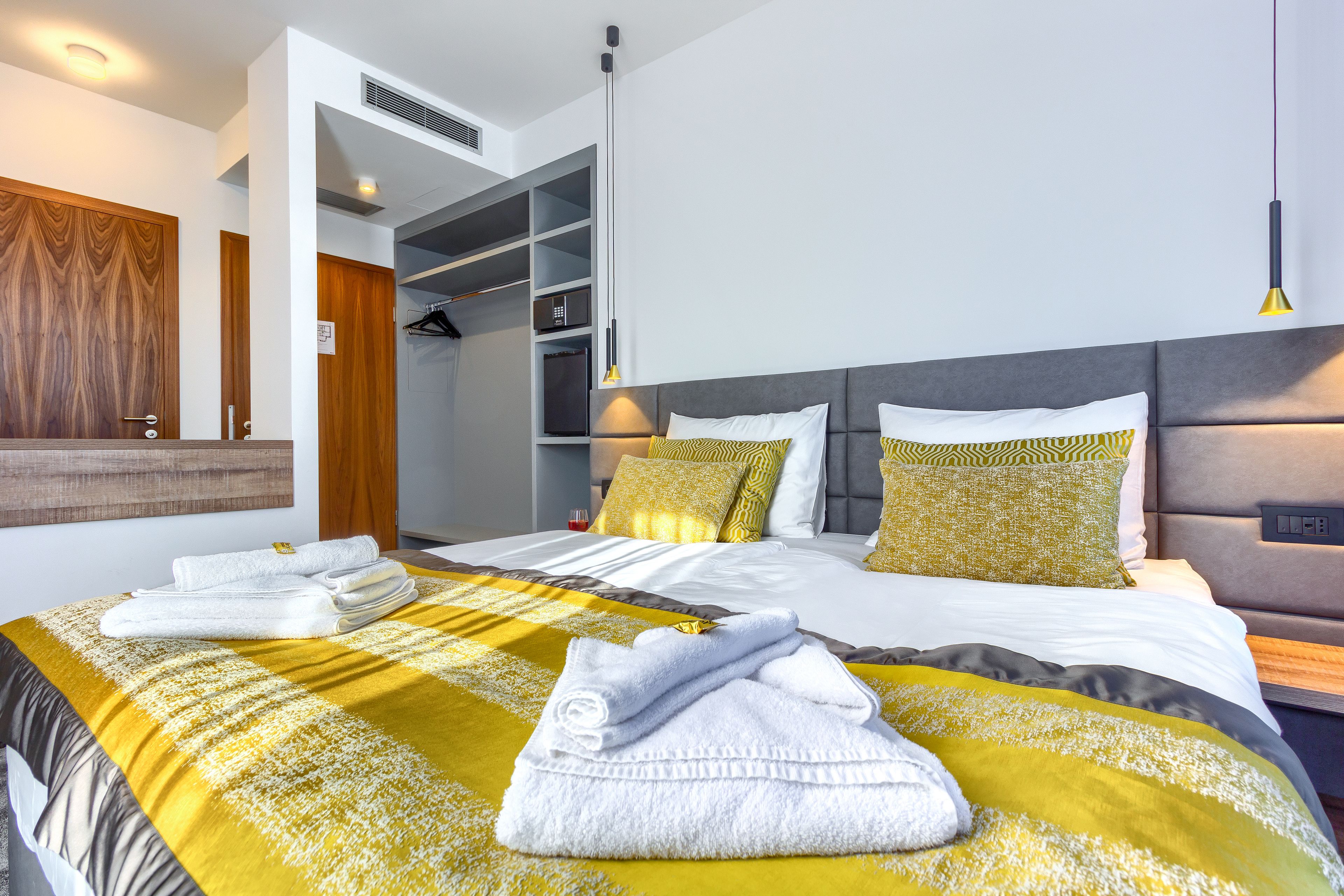 Una habitación de hotel moderna con una cama grande, un vestidor y un baño con espejo y perchero.