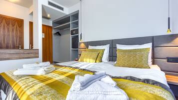 Una habitación de hotel moderna con una cama grande, un vestidor y un baño con espejo y perchero.
