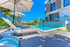 A rooftop pool area with lounge chairs and umbrellas, overlooking a cityscape.