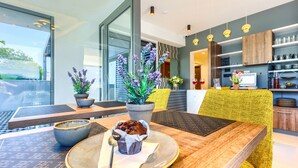 A modern dining area with a wooden table, two potted plants, a muffin on a plate, and a yellow chair. - Bel Residence (Split)