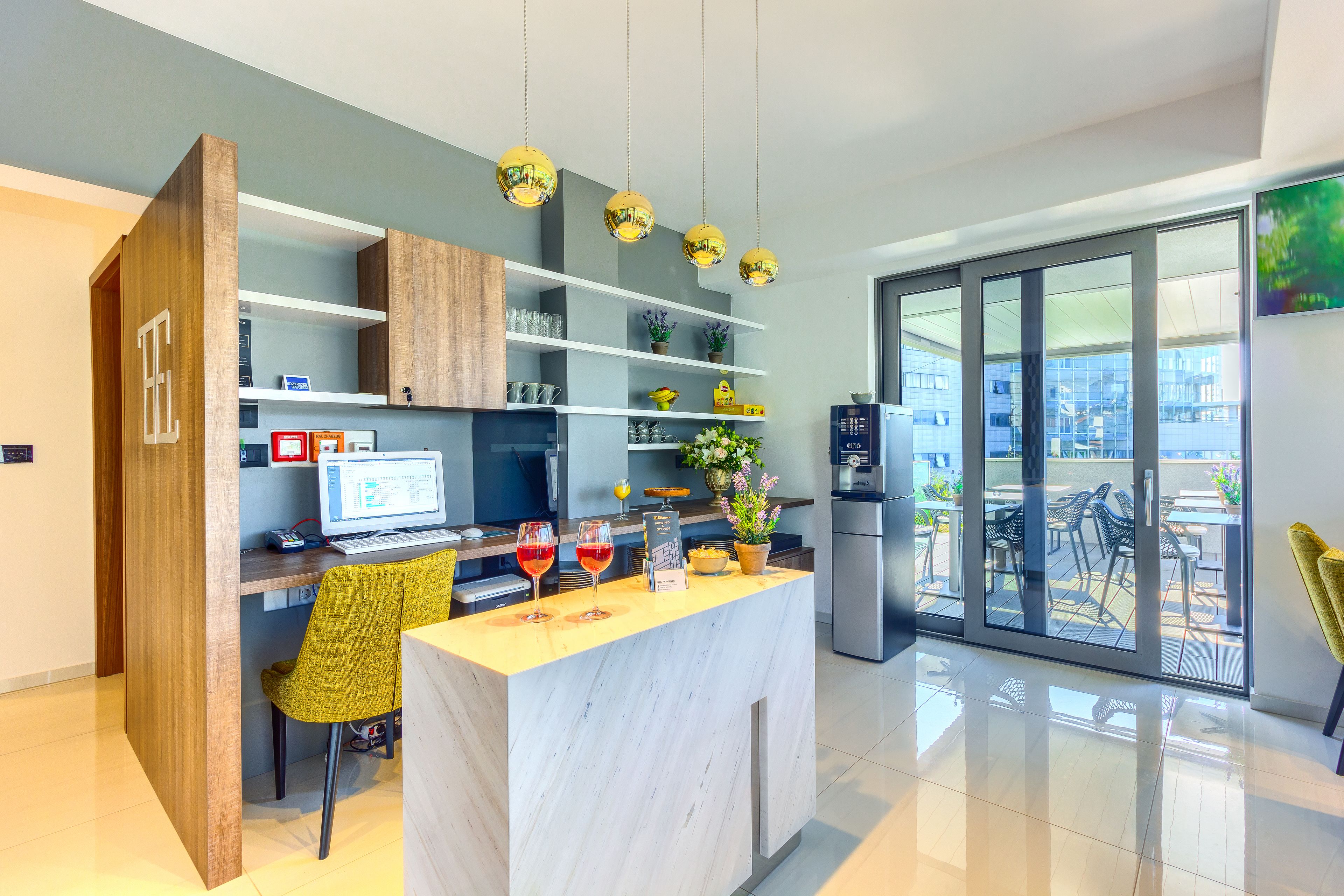 A modern kitchen with a marble countertop, a computer, and wine glasses.