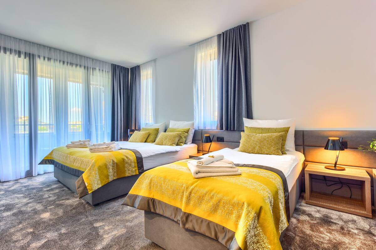 A hotel room with two beds, a nightstand, and a large window with curtains.